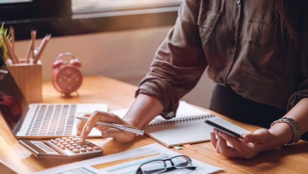 一名办公室职员坐在她的办公桌前，一边使用计算器一边查看手机