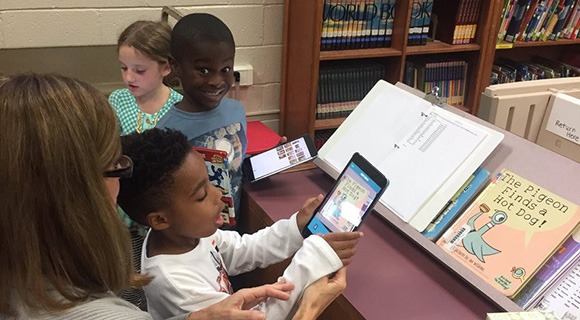 School kids & their teacher interact with a tablet in the library